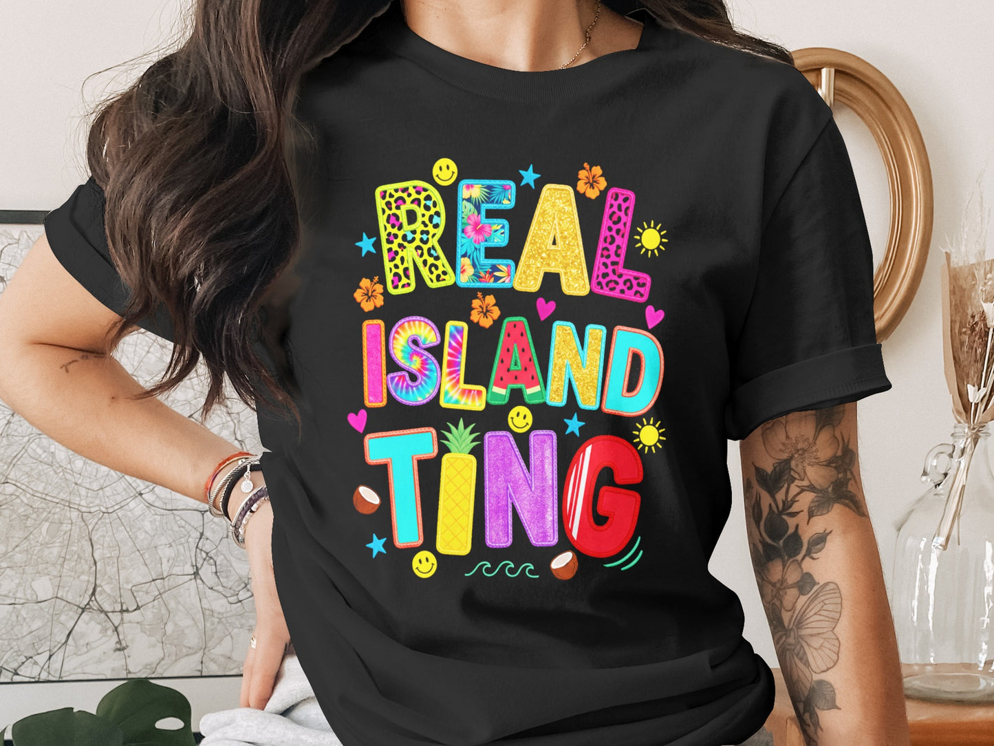 Black t-shirt with "REAL ISLAND TING" text in colorful, playful font.