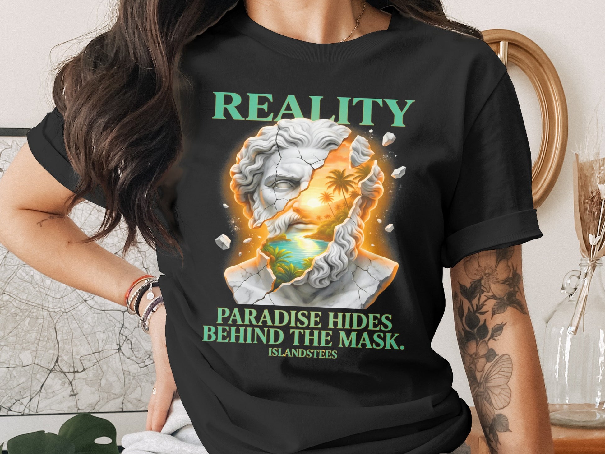 T-shirt graphic of cracked marble bust with tropical scene inside, text reads "REALITY PARADISE HIDES BEHIND THE MASK".