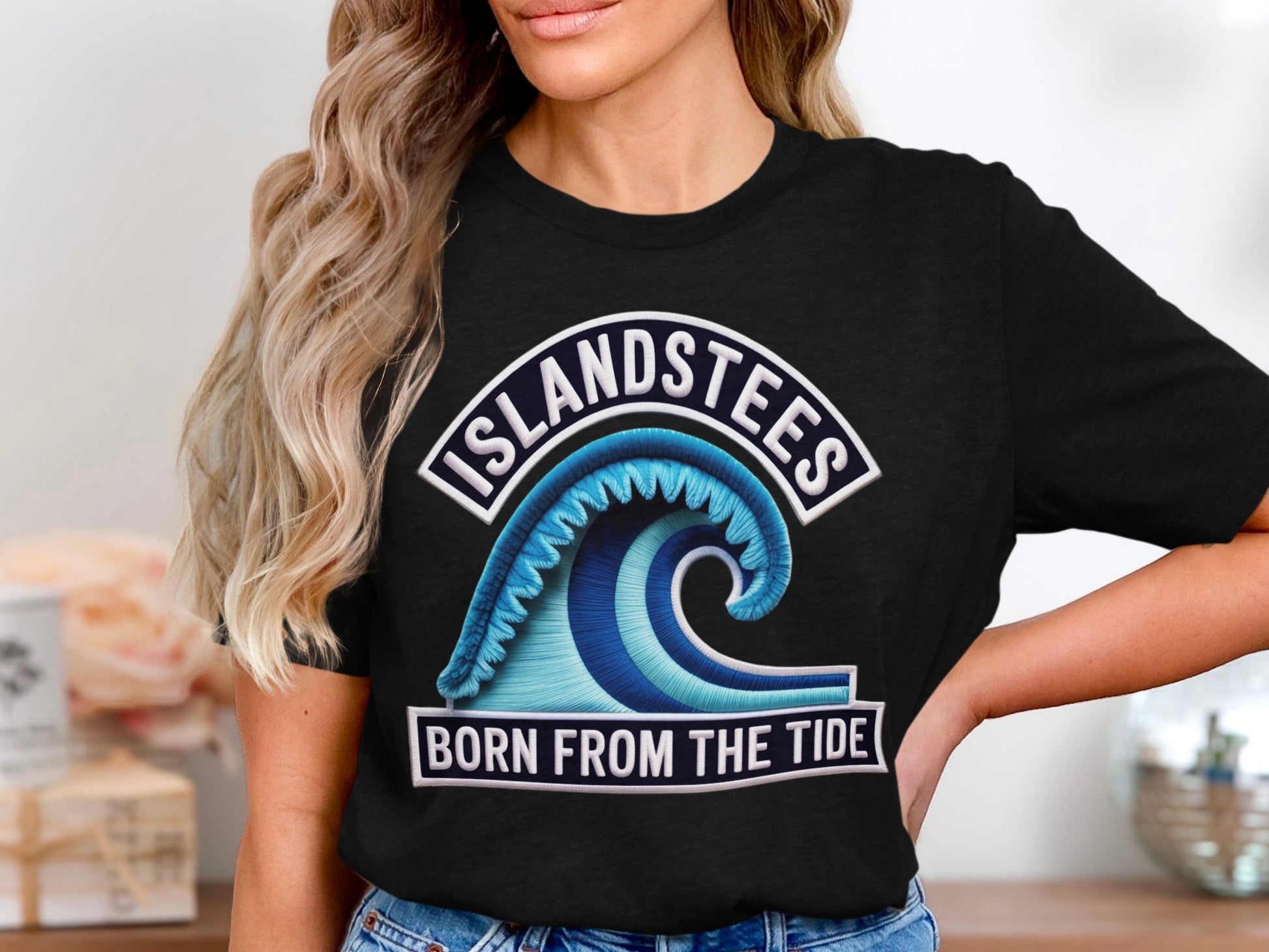 Black t-shirt with "ISLANDSTEES BORN FROM THE TIDE" and a blue ocean wave logo.