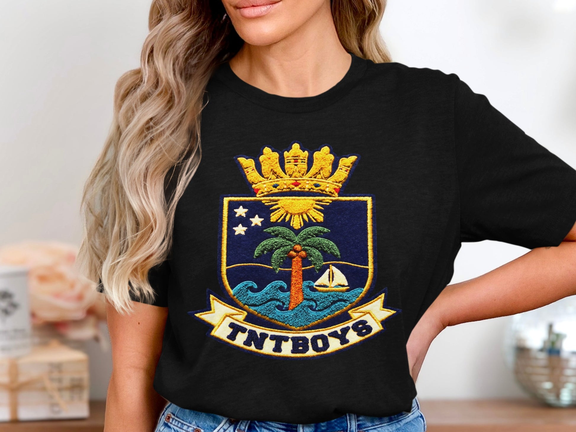 T-shirt with a crest featuring a palm tree, sailing boat, waves, sun, stars, and text TNTBOYS.