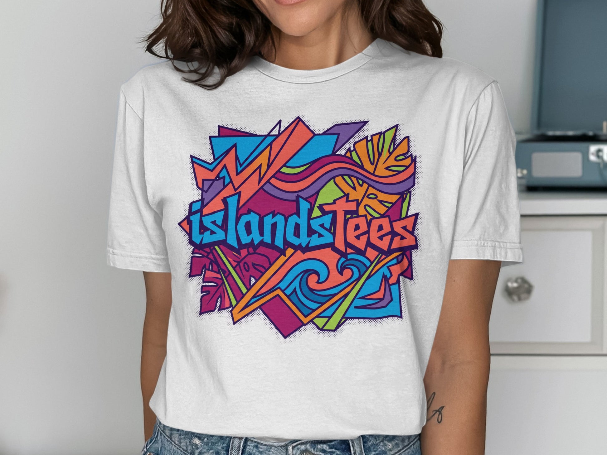 White t-shirt with "ISLANDSTEES" in colorful graffiti-style lettering and abstract shapes.